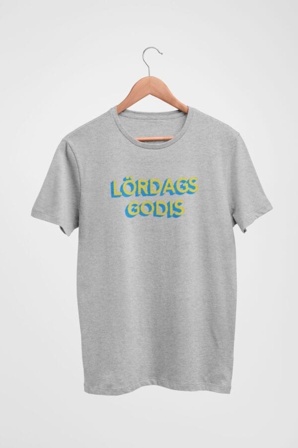 The Lordagsgodis T-Shirt on a wooden hanger features "LÖRDAGS GODIS" in bold, wavy blue and yellow letters against a plain white background.